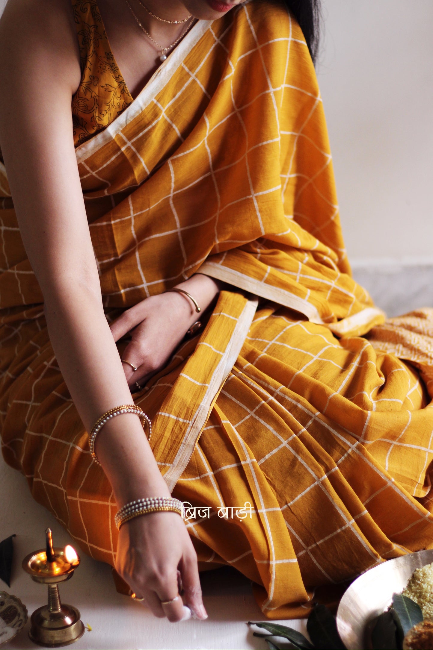 Yellow soft and light-weight cotton saree by Brij Bari, hand block printed in white with a classic check pattern on the body and a striking geometrical pattern on the pallu. Detailed with pink handmade thread tassels that add a charming, handcrafted touch. This saree comes with a free matching block printed blouse piece, offering a complete, artisanal look. A versatile, breathable saree perfect for everyday wear, casual outings, or semi-formal occasions, with free shipping pan India. Available in 2 colours
