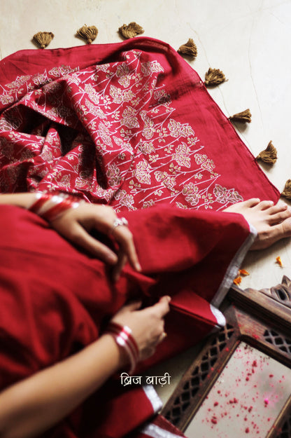 Deep red light-weight cotton saree by Brij Bari, featuring an intricately hand block printed floral pattern in gold and silver on the pallu. The saree is designed with a minimalist border for a timeless appeal, and the pallu is adorned with handcrafted olive green thread tassels that add a unique, earthy contrast. A versatile and comfortable pick for the festive season, it comes with a free matching hand block printed blouse piece. Thoughtfully crafted for elegance, ease, and tradition.

