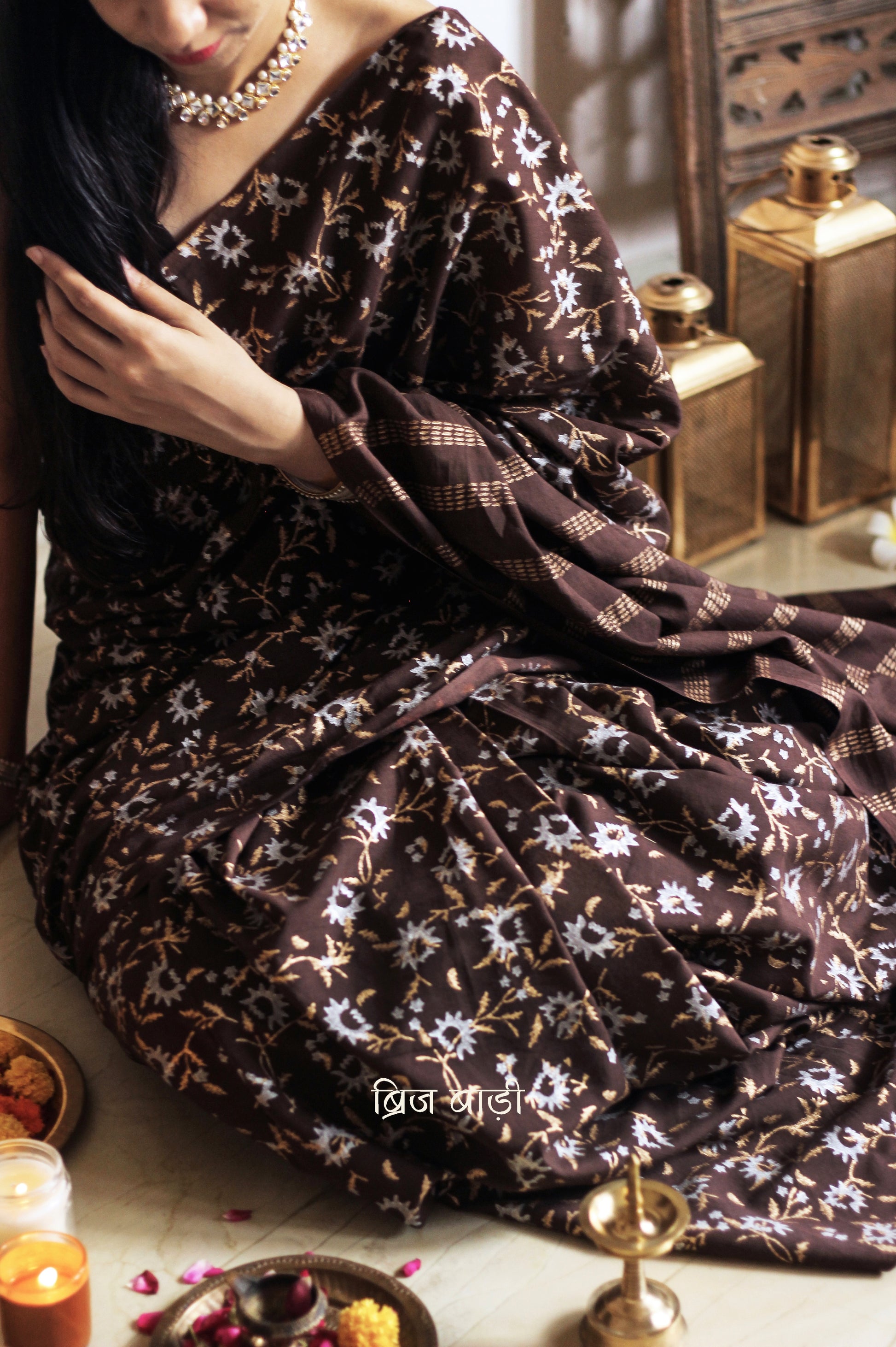 Brown soft cotton saree by Brij Bari, adorned with an abstract floral hand block print in elegant shades of gold and silver, lending it a refined festive charm. Crafted from breathable, light-weight cotton, the saree is accented with handcrafted mustard thread tassels on the pallu for a warm, artisanal finish. It comes with a free hand block printed blouse piece that complements the overall design. Ideal for festive occasions, this saree blends traditional techniques with modern aesthetics