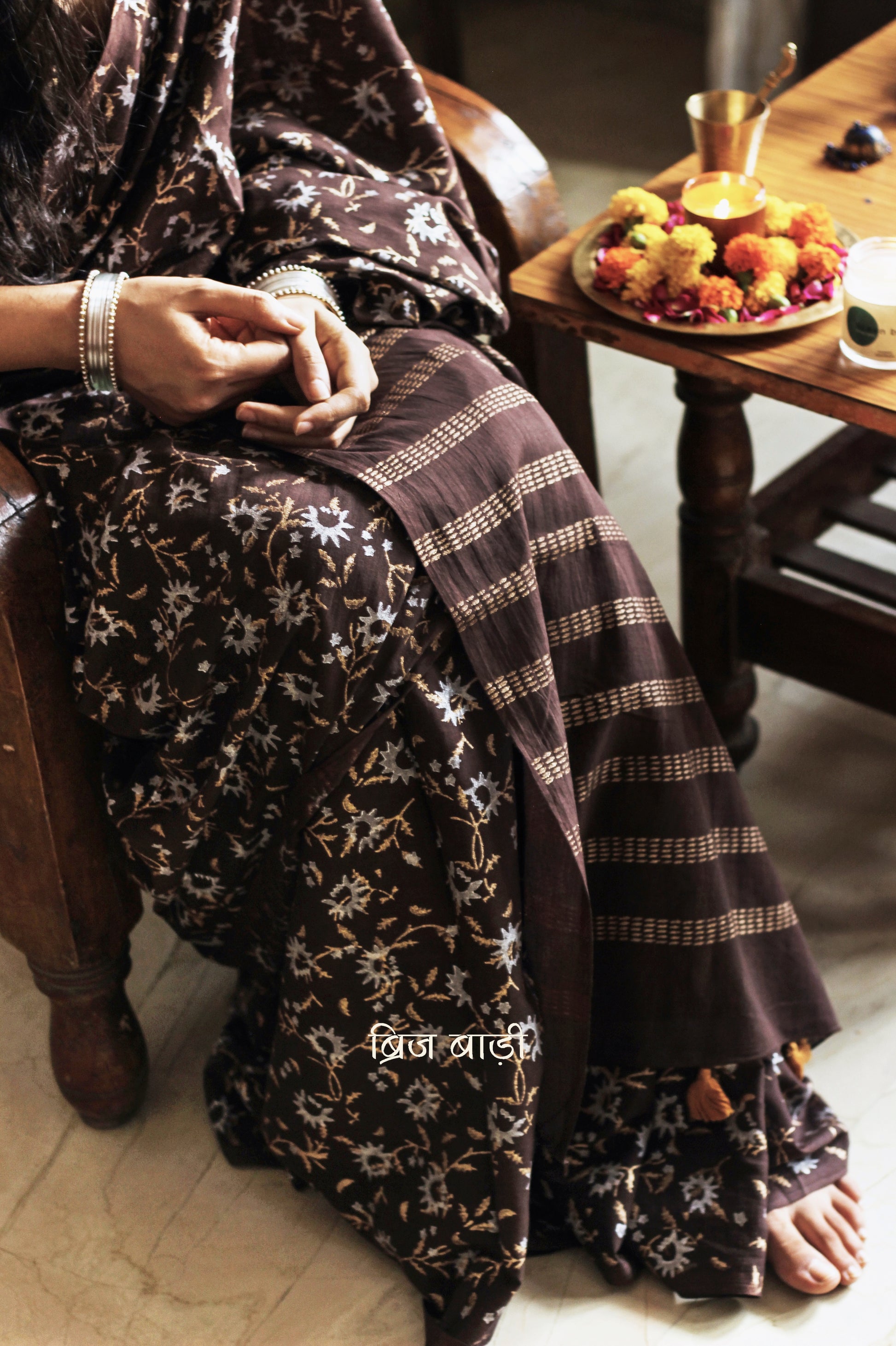 Brown soft cotton saree by Brij Bari, adorned with an abstract floral hand block print in elegant shades of gold and silver, lending it a refined festive charm. Crafted from breathable, light-weight cotton, the saree is accented with handcrafted mustard thread tassels on the pallu for a warm, artisanal finish. It comes with a free hand block printed blouse piece that complements the overall design. Ideal for festive occasions, this saree blends traditional techniques with modern aesthetics