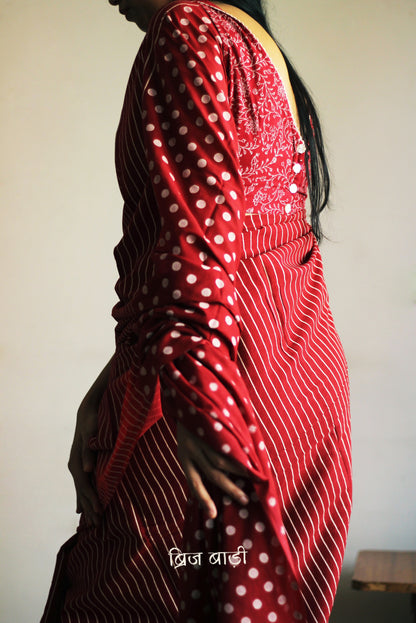 Deep Red soft cotton saree by Brij Bari, featuring a bold and striking hand block printed pattern of stripes and polka dots for a modern, playful twist. Crafted from breathable, light-weight cotton, the saree drapes effortlessly—ideal for both everyday wear and special occasions. Finished with handcrafted light green thread tassels on the pallu, adding an artisanal touch of charm. It comes with a free hand block printed blouse piece that complements the print and palette. 