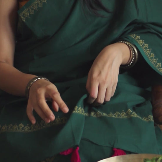 Deep green soft and light-weight cotton saree by Brij Bari, featuring a delicate hand block printed border in vibrant ochre yellow that contrasts beautifully with the rich green. The saree is finished with pink handmade thread tassels on the pallu, adding a touch of traditional charm. It comes with a free matching block printed blouse piece, completing the handcrafted look. Perfect for everyday wear, casual outings, or semi-formal occasions, with free shipping pan India.