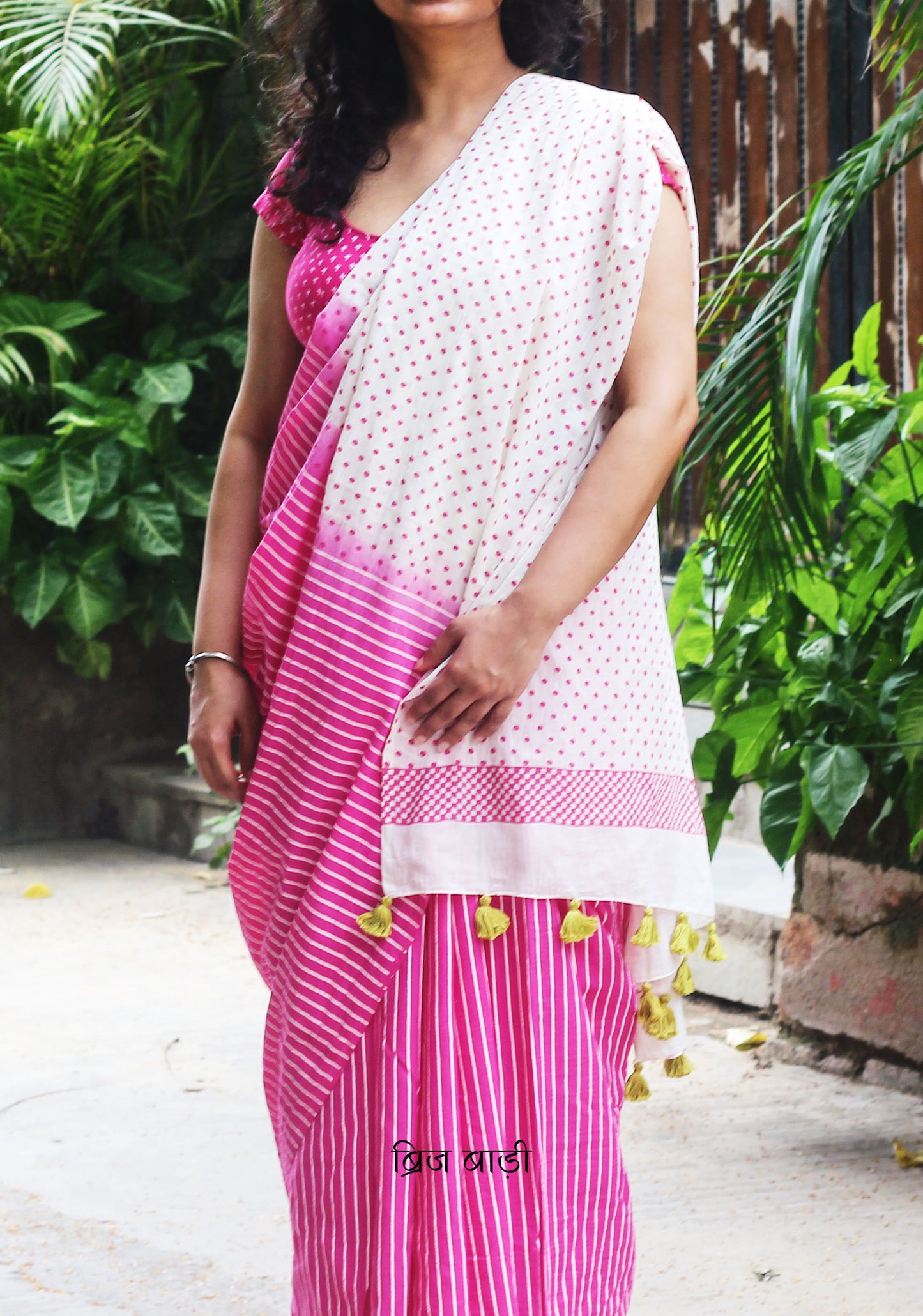 Off-white and pink ombré soft cotton saree by Brij Bari, featuring a bold and striking hand block printed pattern of stripes and polka dots for a modern, playful twist. Crafted from breathable, light-weight cotton, the saree drapes effortlessly—ideal for both everyday wear and special occasions. Finished with handcrafted light green thread tassels on the pallu, adding an artisanal touch of charm. It comes with a free hand block printed blouse piece that complements the print and palette. 