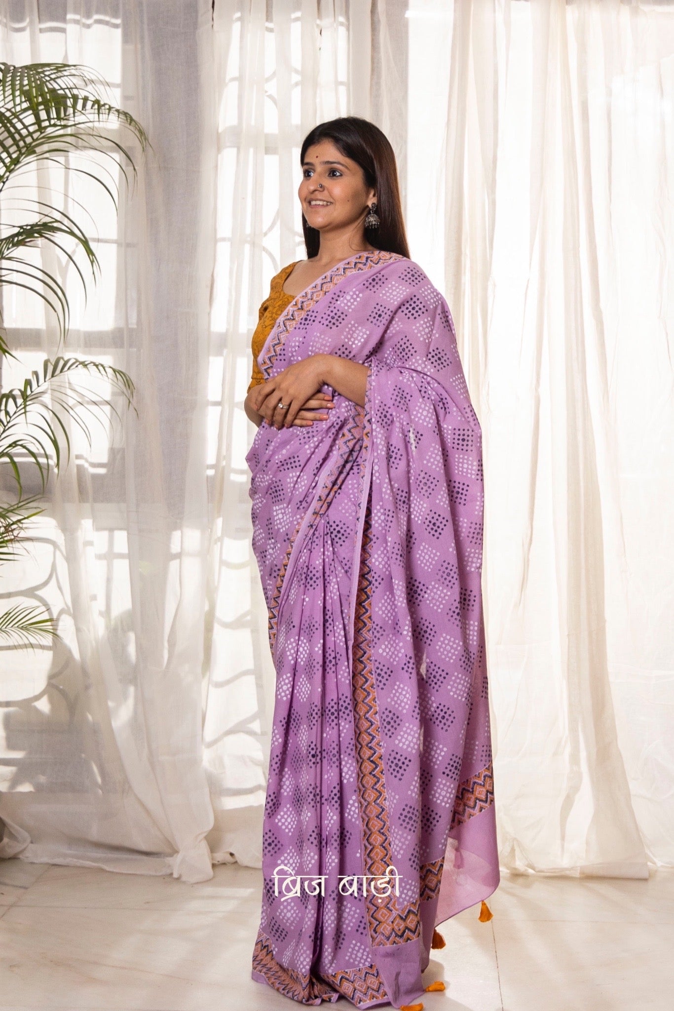 Lavender buttery soft and light-weight cotton saree by Brij Bari, featuring a playful polka dot pattern hand block printed in blue and yellow on the pallu. The saree is detailed with orange handmade thread tassels on the pallu, adding a pop of color. It comes with a free block printed blouse piece, making it a versatile option for everyday wear and casual occasions. Designed for all-day comfort and style, with free shipping available pan India.