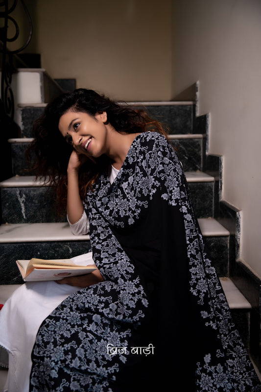 Black soft and light-weight cotton dupatta by Brij Bari, adorned with an elegant floral border hand block printed in crisp white, creating a striking contrast against the deep black base. Crafted from breathable, airy cotton fabric, this dupatta is ideal to pair with suits, kurtas, or ethnic sets, adding a refined handcrafted touch to both everyday and occasion wear. The pallu is finished with vibrant red handmade thread tassels, offering a playful, artisanal accent to the look. 