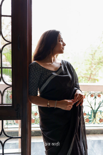 Black soft and light-weight cotton saree by Brij Bari with a simple and elegant hand block printed border in white for a timeless minimal look. Made from breathable, easy-to-drape cotton, this saree is perfect for everyday wear, offering effortless style & comfort. Pallu is finished with handmade mustard thread tassels, adding a handcrafted detail and a pop of colour. Includes a free hand block printed blouse piece designed to complement the sar the saree’s clean, classic border design. 