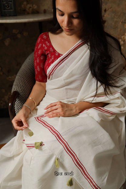 Off-white soft and light-weight cotton saree by Brij Bari with a simple and elegant hand block printed stripe pattern border in rich red. Designed for breathable comfort and effortless everyday style, this saree drapes beautifully for work, casual days or relaxed occasions. The pallu is finished with delicate light green handmade thread tassels adding a subtle artisanal detail. It comes with a free hand block printed blouse piece thoughtfully designed to complement the saree’s minimal design. Free Shipping 