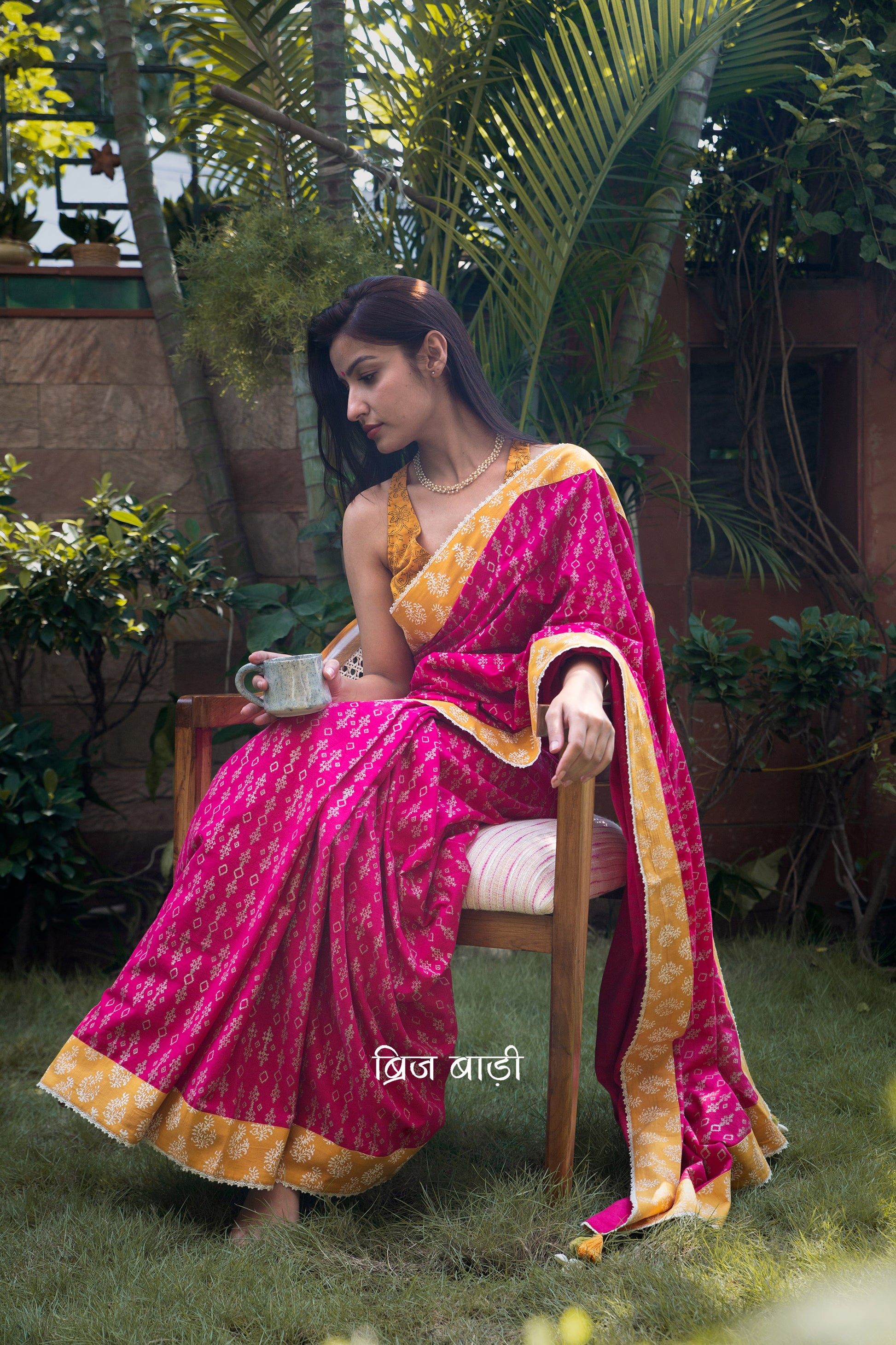 Pink cotton saree by Brij Bari, hand block printed with a delicate geometrical pattern in silver, beautifully contrasted with an ochre yellow block printed border. The saree is finished with fine crochet lace detailing and adorned with handmade orange and light green thread tassels on the pallu corner, accented with decorative sea shells. A standout festive or special occasion saree designed for both style and comfort. Comes with a free block printed blouse piece. Free shipping pan India.