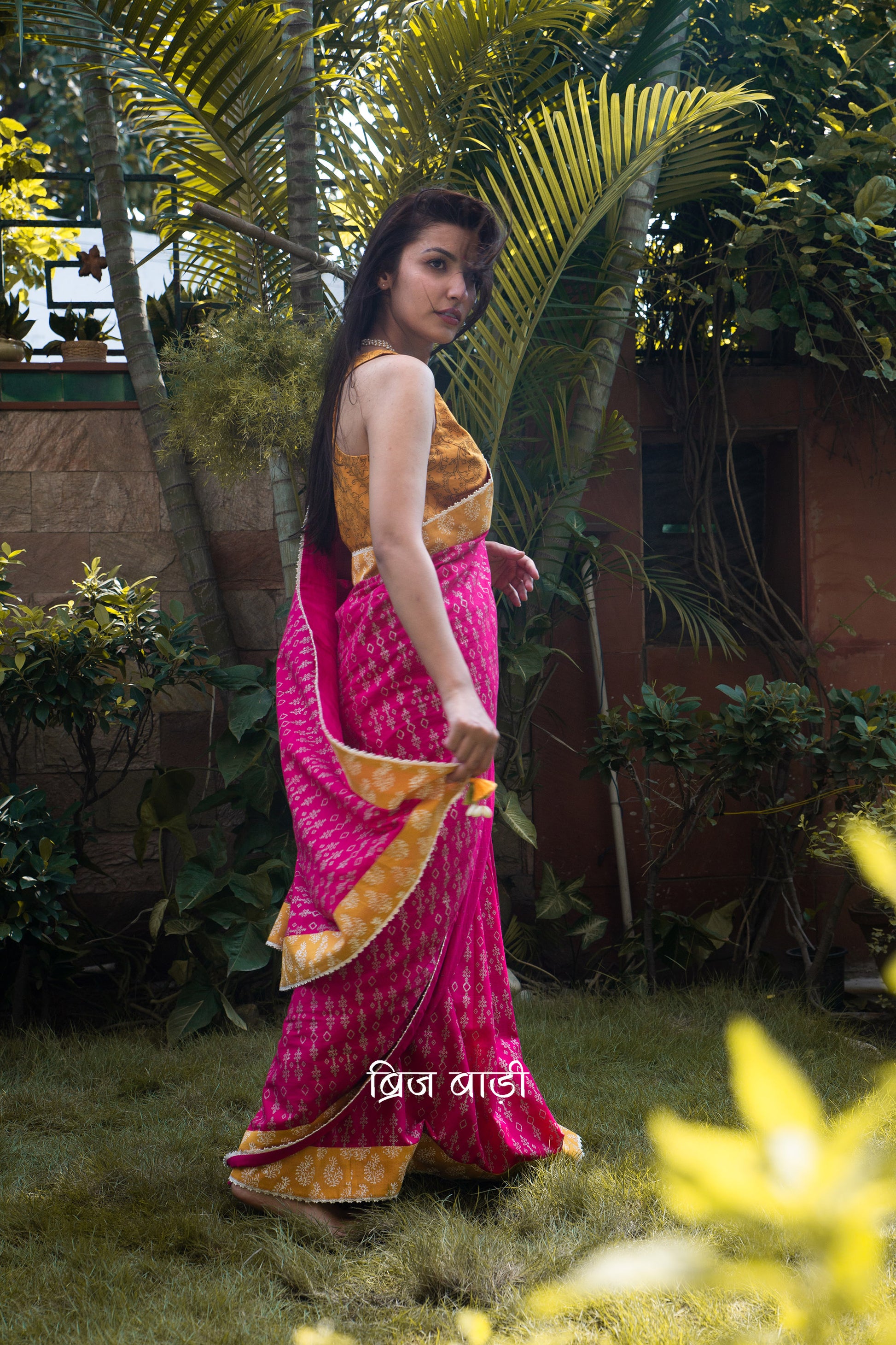 Pink cotton saree by Brij Bari, hand block printed with a delicate geometrical pattern in silver, beautifully contrasted with an ochre yellow block printed border. The saree is finished with fine crochet lace detailing and adorned with handmade orange and light green thread tassels on the pallu corner, accented with decorative sea shells. A standout festive or special occasion saree designed for both style and comfort. Comes with a free block printed blouse piece. Free shipping pan India.