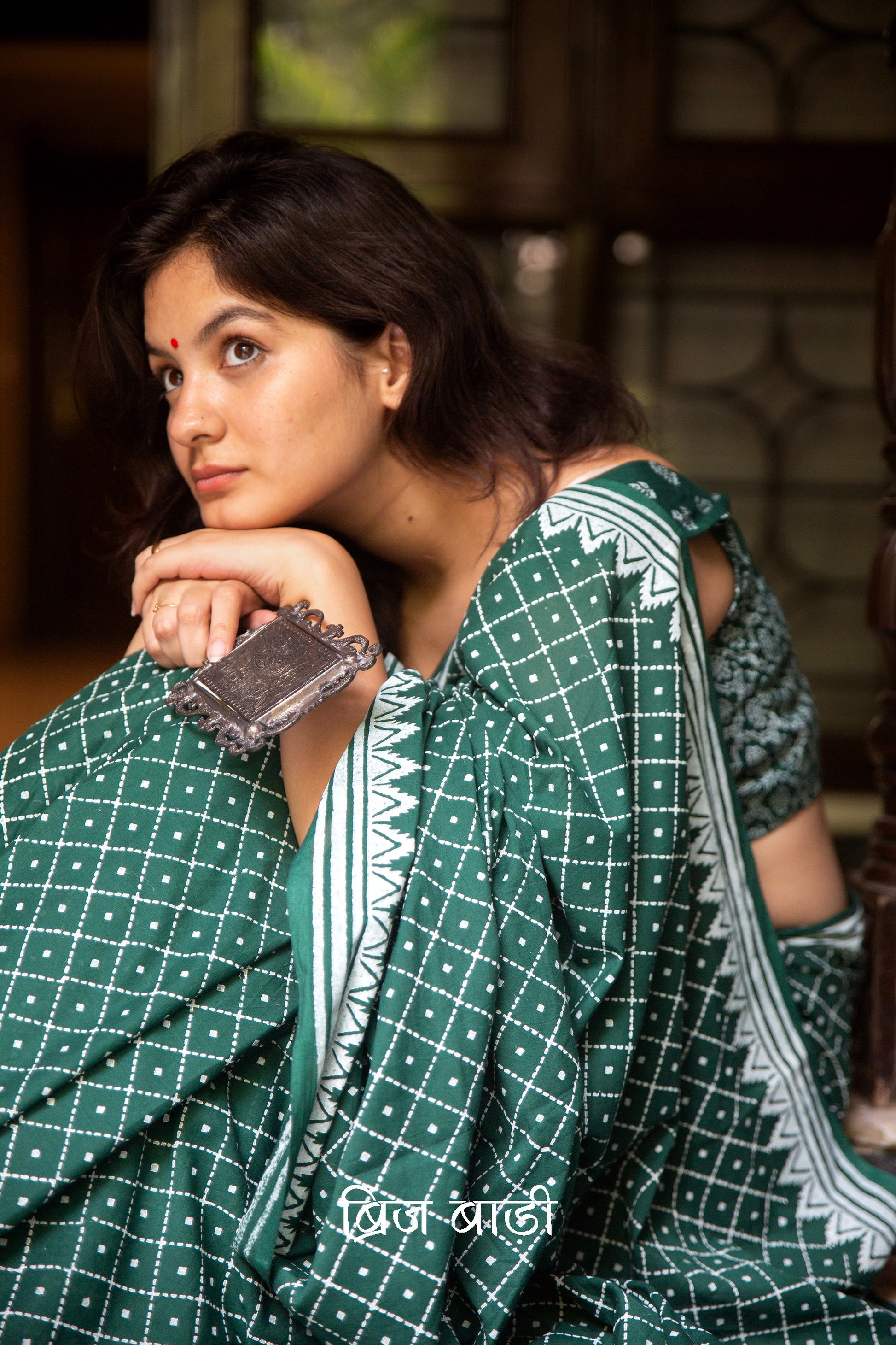Dark green buttery soft and lightweight cotton saree by Brij Bari, hand block printed with an elegant white geometrical pattern. The pallu is accented with handcrafted red thread tassels, adding a vibrant artisanal detail. Includes a matching block printed blouse piece. Designed for all-day comfort and ease, this saree is a stylish and breathable option for everyday elegance. Free shipping pan India.