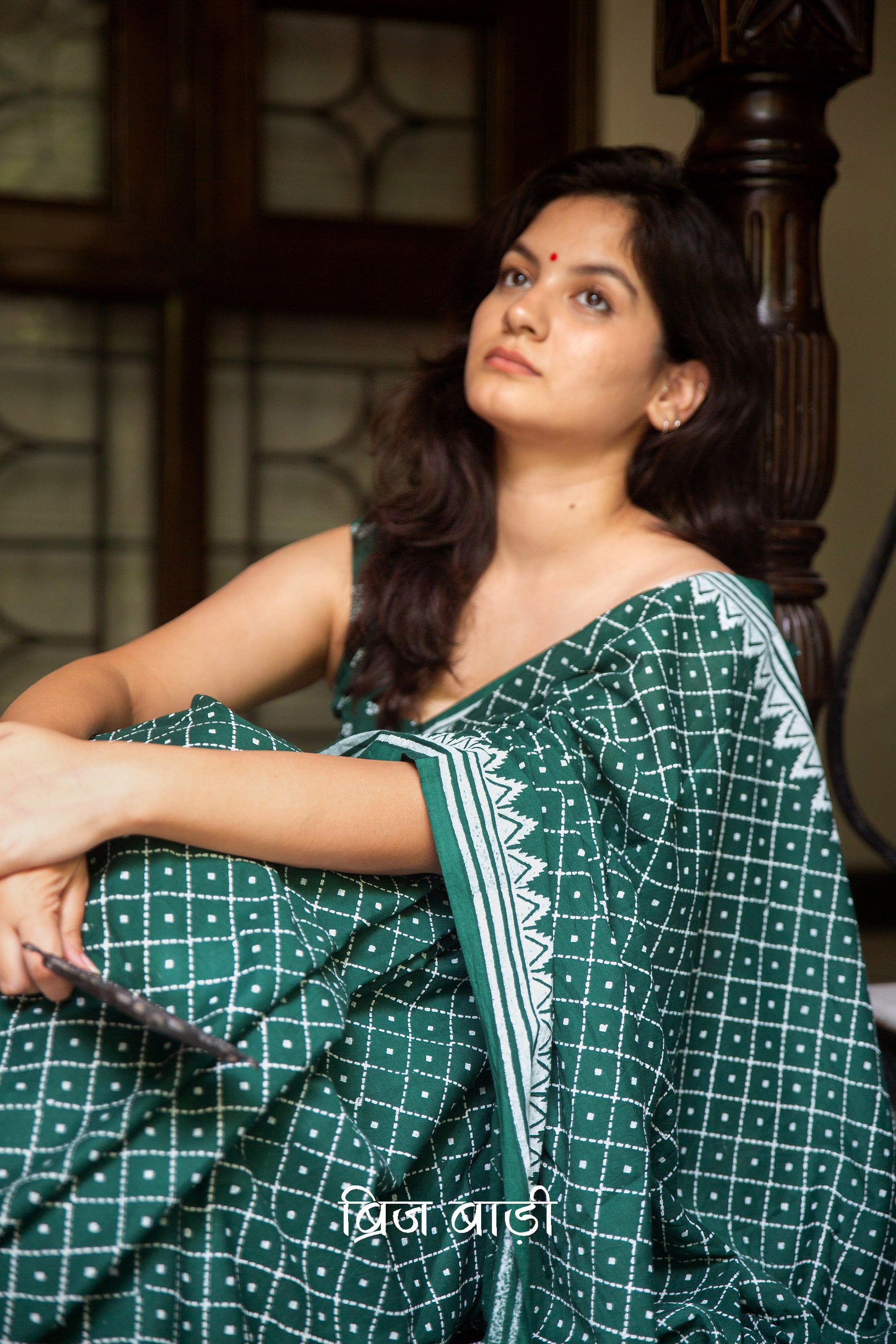 Dark green buttery soft and lightweight cotton saree by Brij Bari, hand block printed with an elegant white geometrical pattern. The pallu is accented with handcrafted red thread tassels, adding a vibrant artisanal detail. Includes a matching block printed blouse piece. Designed for all-day comfort and ease, this saree is a stylish and breathable option for everyday elegance. Free shipping pan India.