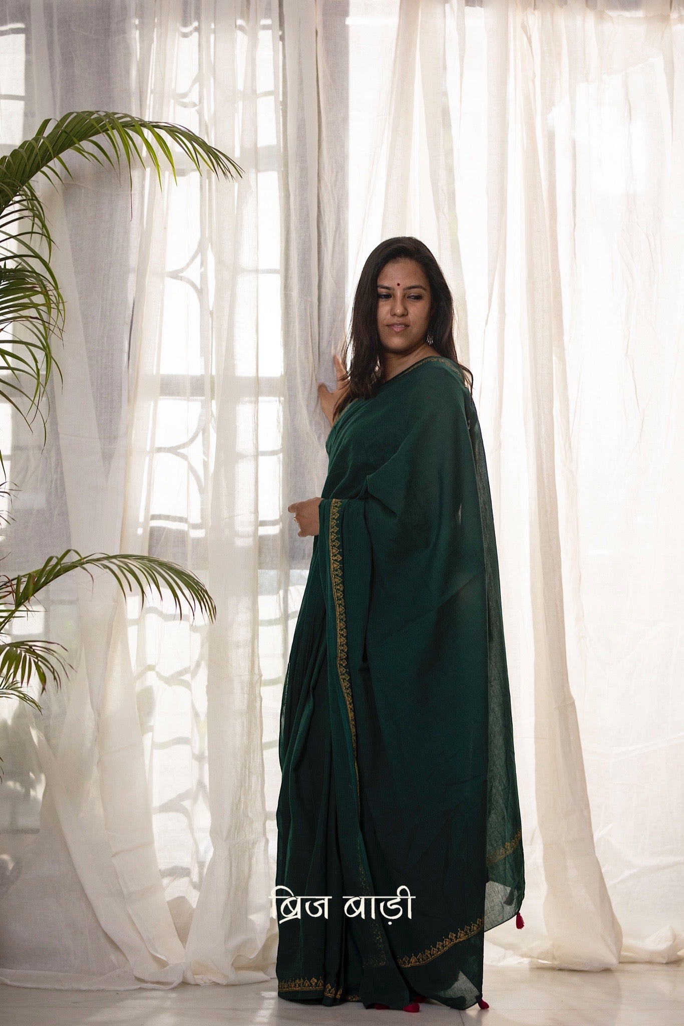 Deep green soft and light-weight cotton saree by Brij Bari, featuring a delicate hand block printed border in vibrant ochre yellow that contrasts beautifully with the rich green. The saree is finished with pink handmade thread tassels on the pallu, adding a touch of traditional charm. It comes with a free matching block printed blouse piece, completing the handcrafted look. Perfect for everyday wear, casual outings, or semi-formal occasions, with free shipping pan India.