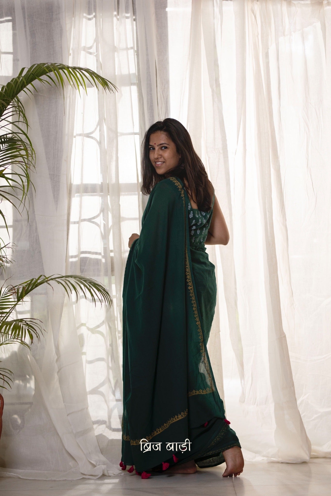 Deep green soft and light-weight cotton saree by Brij Bari, featuring a delicate hand block printed border in vibrant ochre yellow that contrasts beautifully with the rich green. The saree is finished with pink handmade thread tassels on the pallu, adding a touch of traditional charm. It comes with a free matching block printed blouse piece, completing the handcrafted look. Perfect for everyday wear, casual outings, or semi-formal occasions, with free shipping pan India.