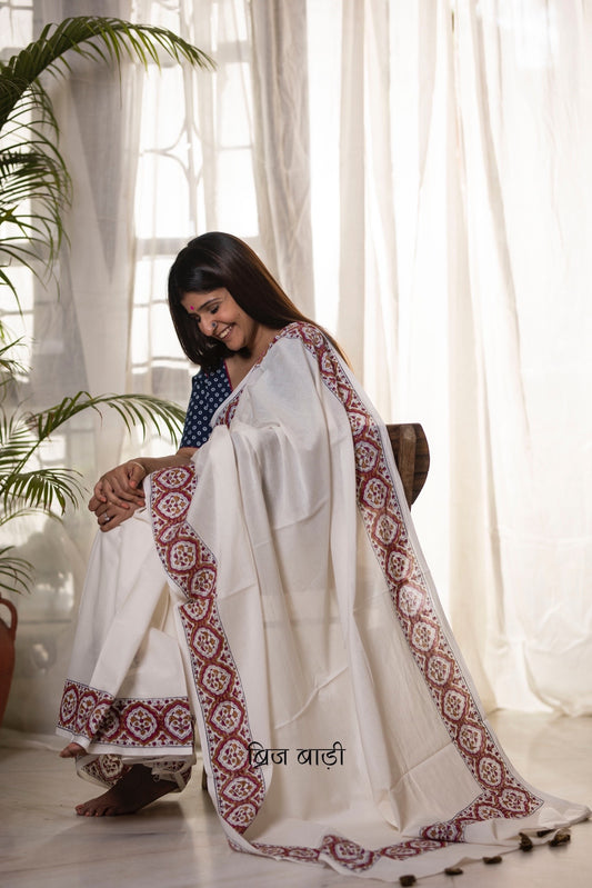 Off white soft and light-weight cotton saree by Brij Bari, featuring a delicate and intricate multicolour hand block printed border crafted by skilled artisans. Designed for all-day comfort and effortless style, this saree is detailed with olive green handmade thread tassels on the pallu. It comes with a free block printed blouse piece, making it a versatile pick for everyday wear, casual gatherings, and relaxed festive occasions. Free shipping pan India.