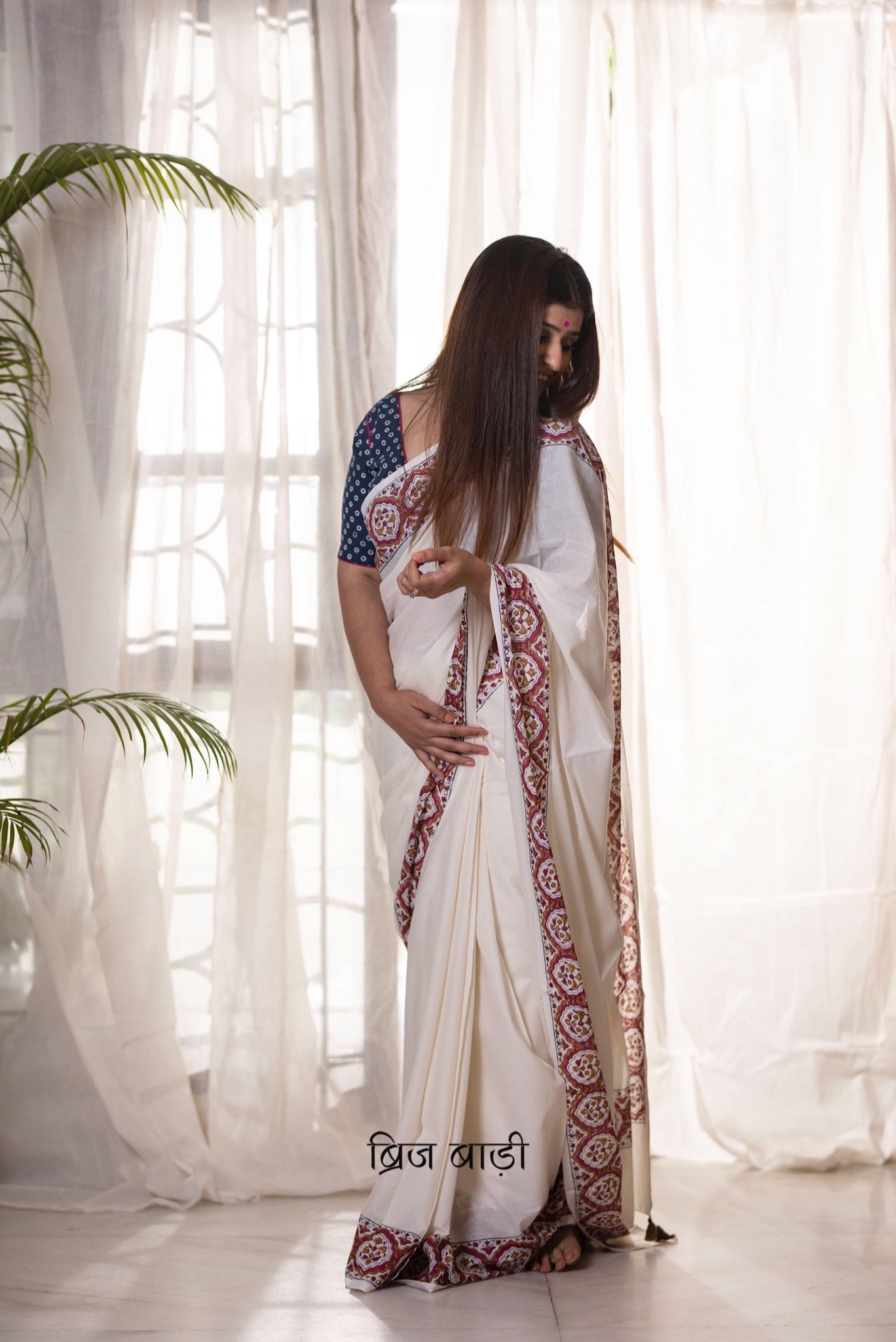 Off white soft and light-weight cotton saree by Brij Bari, featuring a delicate and intricate multicolour hand block printed border crafted by skilled artisans. Designed for all-day comfort and effortless style, this saree is detailed with olive green handmade thread tassels on the pallu. It comes with a free block printed blouse piece, making it a versatile pick for everyday wear, casual gatherings, and relaxed festive occasions. Free shipping pan India.