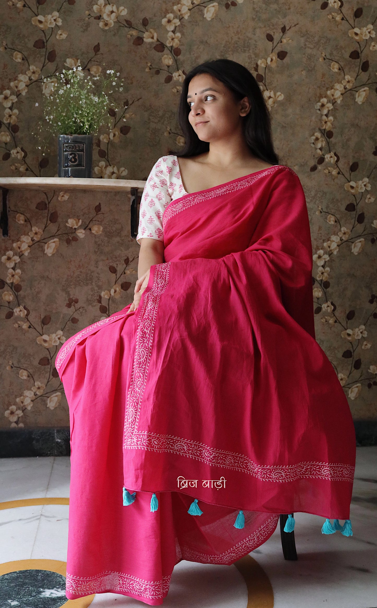 Pink soft and light-weight cotton saree by Brij Bari witha simple & elegant hand block printed border in classic white for a fresh, minimal appeal. Crafted from breathable, airy cotton, this saree is perfect for everyday wear — easy to drape, comfortable for the summer, and effortlessly stylish for work or casual outings. The pallu is finished with striking red handmade thread tassels, adding a handcrafted artisanal touch. Comes with a free hand block printed blouse piece.