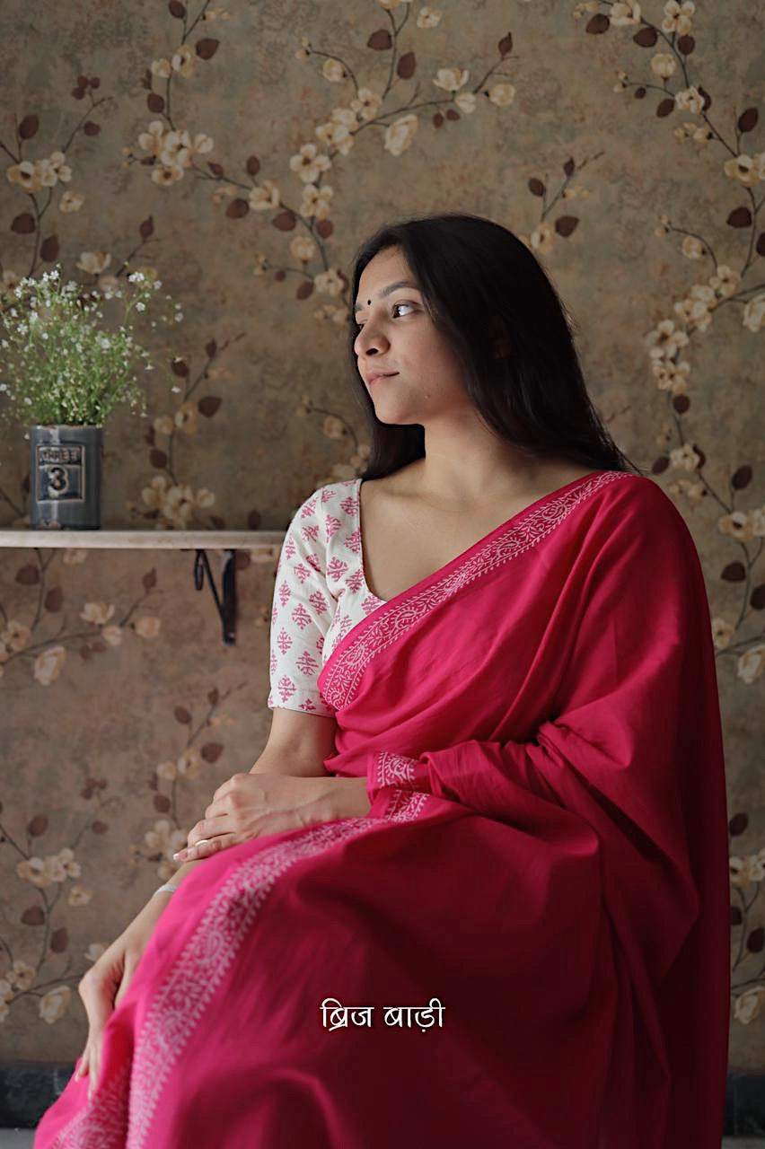 Pink soft and light-weight cotton saree by Brij Bari witha simple & elegant hand block printed border in classic white for a fresh, minimal appeal. Crafted from breathable, airy cotton, this saree is perfect for everyday wear — easy to drape, comfortable for the summer, and effortlessly stylish for work or casual outings. The pallu is finished with striking red handmade thread tassels, adding a handcrafted artisanal touch. Comes with a free hand block printed blouse piece.