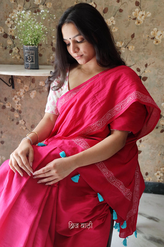 Pink soft and light-weight cotton saree by Brij Bari witha simple & elegant hand block printed border in classic white for a fresh, minimal appeal. Crafted from breathable, airy cotton, this saree is perfect for everyday wear — easy to drape, comfortable for the summer, and effortlessly stylish for work or casual outings. The pallu is finished with striking red handmade thread tassels, adding a handcrafted artisanal touch. Comes with a free hand block printed blouse piece.