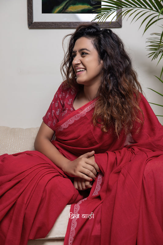 Deep red soft and light-weight cotton saree by Brij Bari with a delicate white hand block printed border. Detailed with mustard handmade thread tassels on the pallu and paired with a free block printed blouse piece. A versatile, breathable saree perfect for everyday wear, with free shipping pan India.