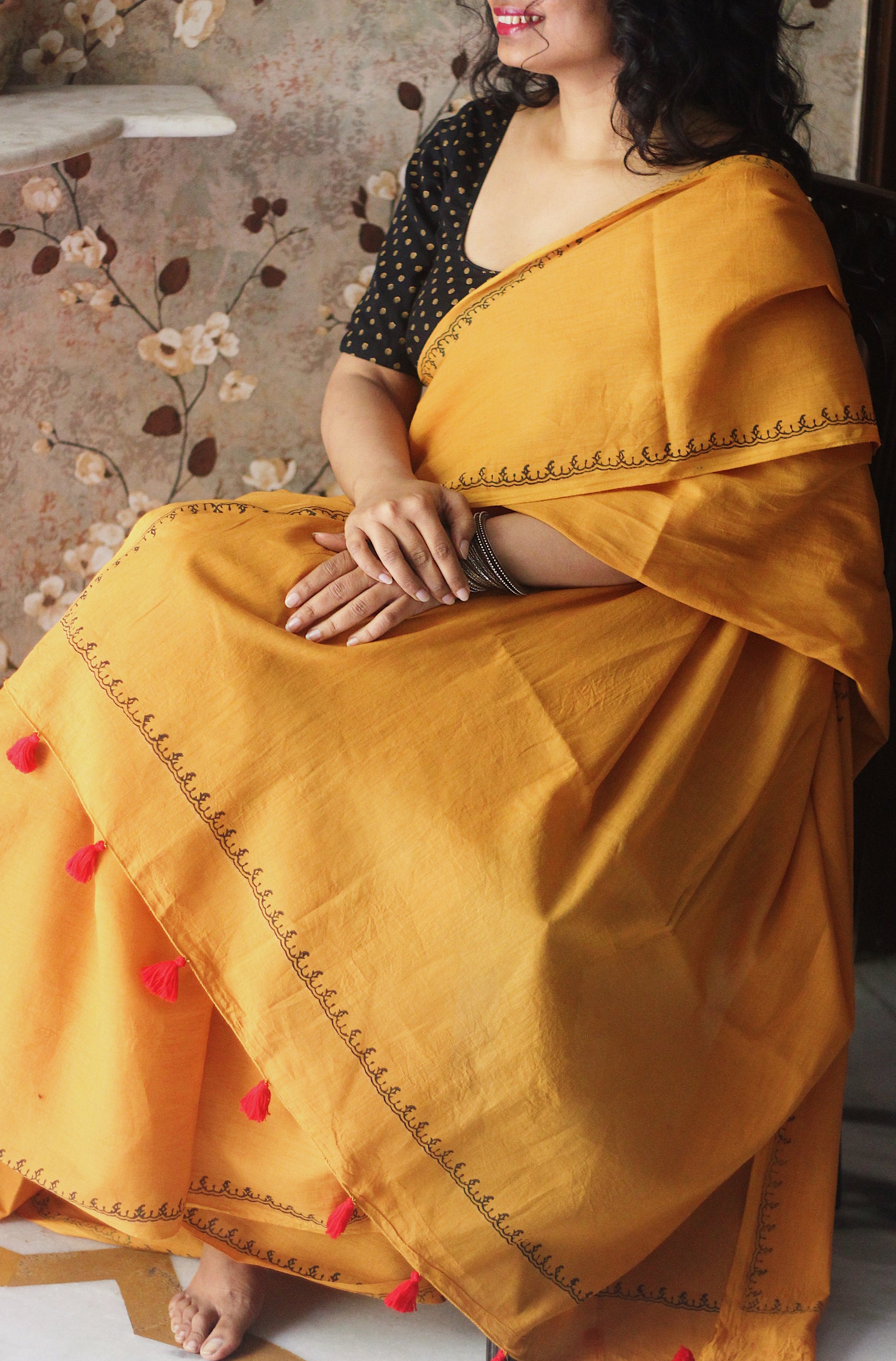 Yellow soft and light-weight cotton saree by Brij Bari hand block printed with a simple and elegant border pattern in classic black for a clean, timeless look. Crafted from breathable this saree is perfect for everyday wear easy to drape, comfortable for warm weather and effortlessly stylish. The pallu is adorned with delicate light green handmade thread tassels adding a fresh handcrafted touch to the design. Paired with a free hand block printed blouse piece carefully coordinated to match the saree