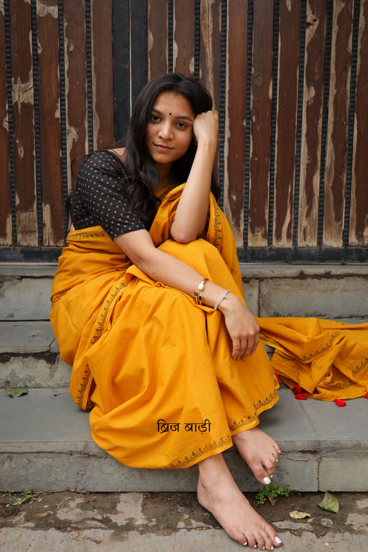 Yellow soft and light-weight cotton saree by Brij Bari hand block printed with a simple and elegant border pattern in classic black for a clean timeless look. Crafted from breathable this saree is perfect for everyday wear easy to drape, comfortable for warm weather and effortlessly stylish. The pallu is adorned with delicate light green handmade thread tassels adding a fresh handcrafted touch to the design. Paired with a free hand block printed blouse piece carefully coordinated to match the saree