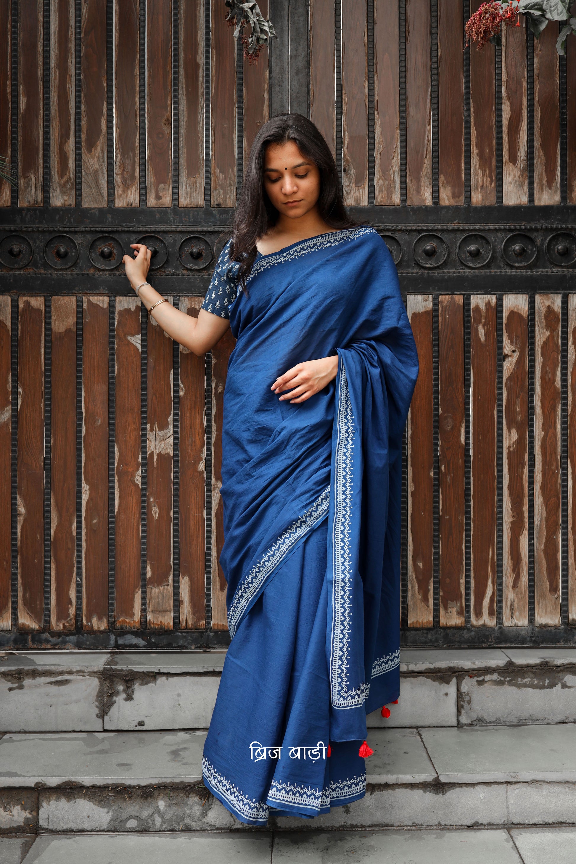Blue soft and light-weight cotton saree by Brij Bari hand block printed with an elegant white border pattern that lends a timeless, understated charm. Made from breathable cotton fabric, this saree ensures day-long comfort making it perfect for everyday wear, work or casual outings. The pallu is adorned with bright red handmade thread tassels adding a vibrant handcrafted accent to the look. It comes with a free hand block printed blouse piece.  Free shipping pan India.
 