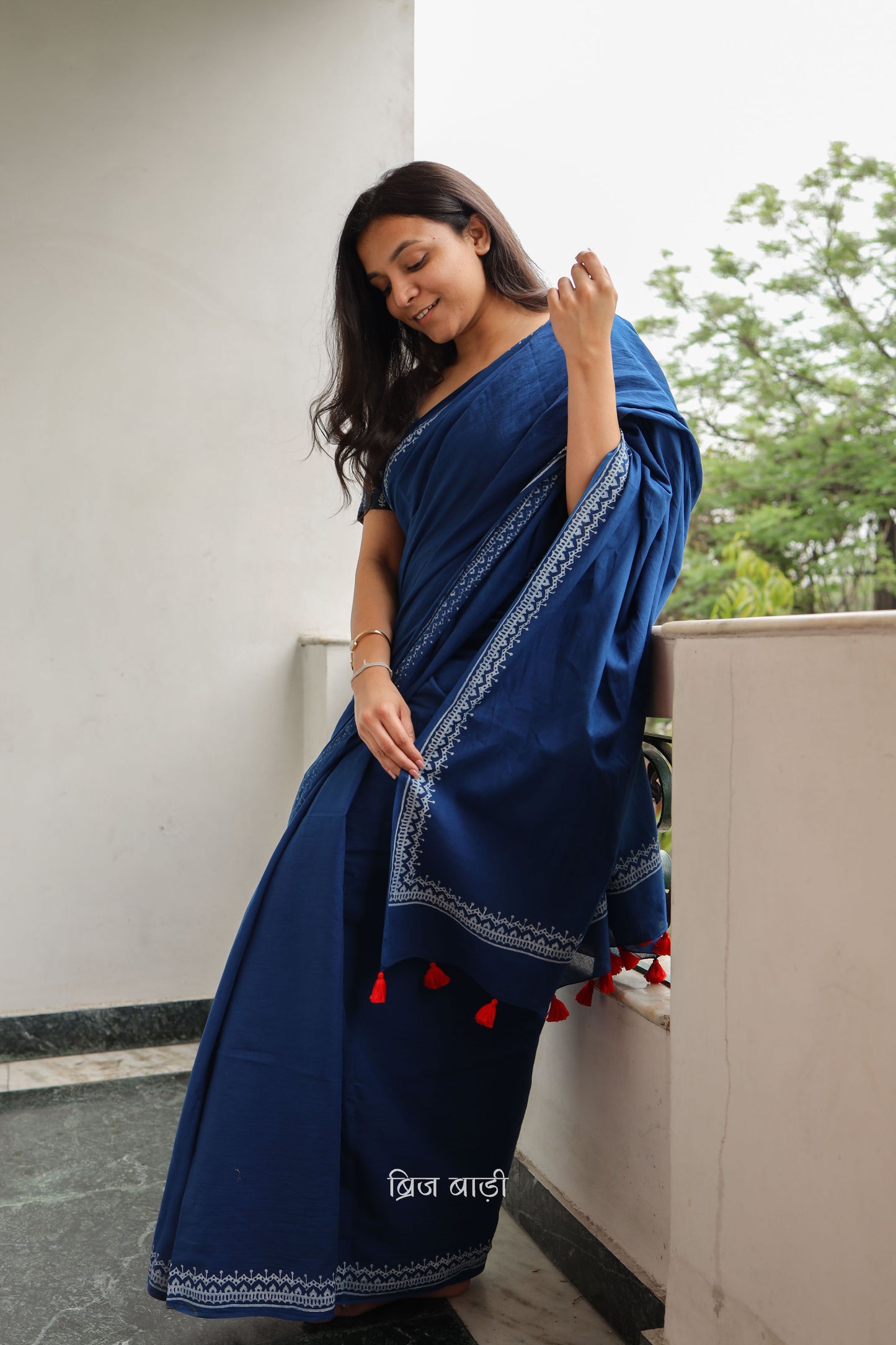 Blue soft and light-weight cotton saree by Brij Bari hand block printed with an elegant white border pattern that lends a timeless, understated charm. Made from breathable cotton fabric, this saree ensures day-long comfort making it perfect for everyday wear, work or casual outings. The pallu is adorned with bright red handmade thread tassels adding a vibrant handcrafted accent to the look. It comes with a free hand block printed blouse piece.  Free shipping pan India.
 