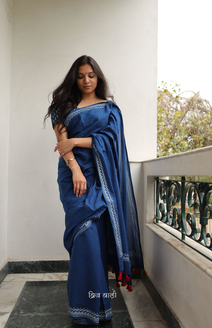 Blue soft and light-weight cotton saree by Brij Bari hand block printed with an elegant white border pattern that lends a timeless, understated charm. Made from breathable cotton fabric, this saree ensures day-long comfort making it perfect for everyday wear, work or casual outings. The pallu is adorned with bright red handmade thread tassels adding a vibrant handcrafted accent to the look. It comes with a free hand block printed blouse piece.  Free shipping pan India.
 