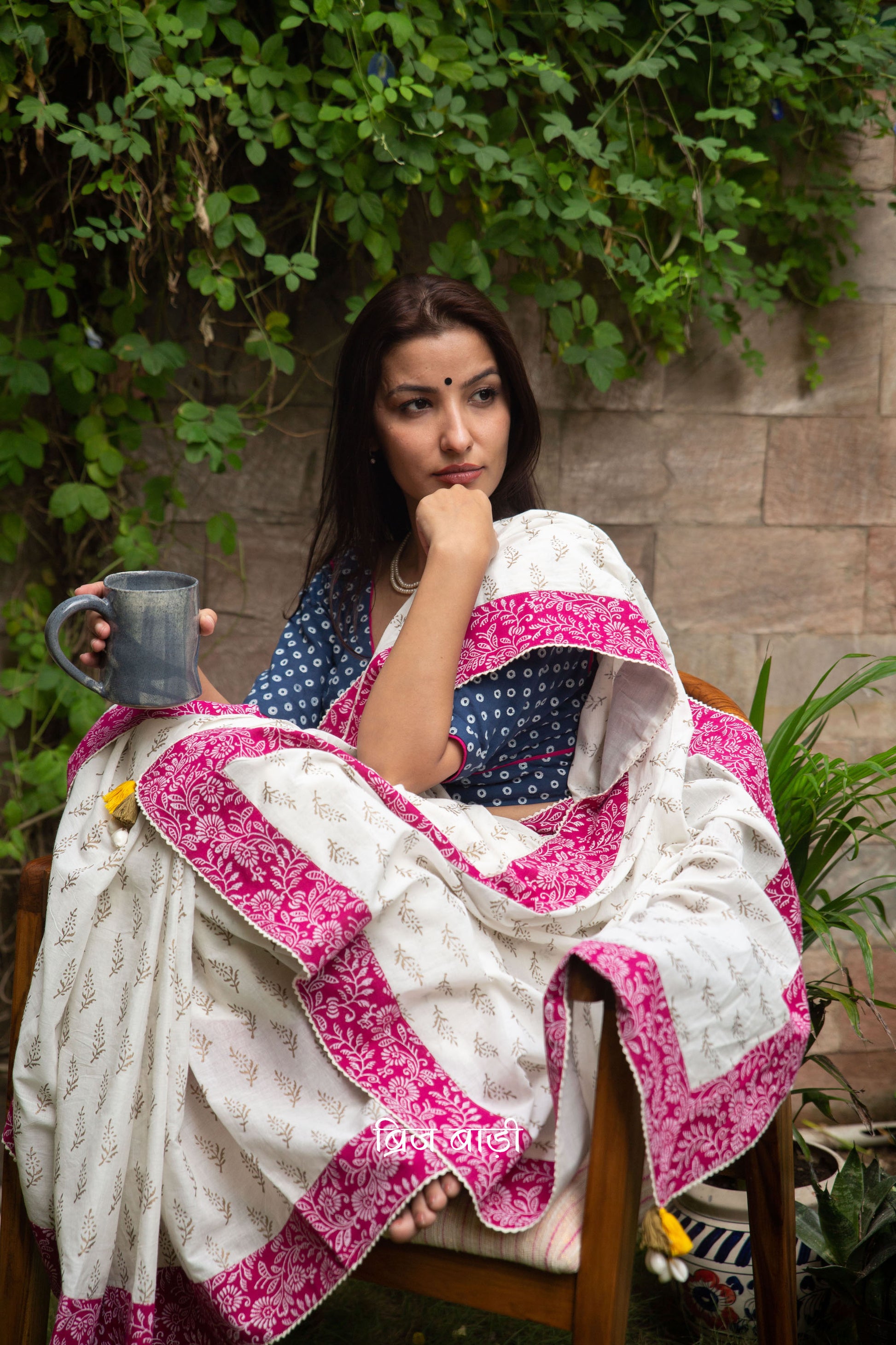 Off white soft cotton saree by Brij Bari hand block printed with intricate gold floral motifs & beautifully contrasted with a pink block printed border. Finished with delicate crochet detailing & adorned with yellow & light green handmade thread tassels accented with sea shells on pallu corner. Comes with matching block printed blouse piece. Perfect pick for festive or special occasions designed to make you stand out while staying effortlessly comfortable through long celebrations. Free shipping pan India