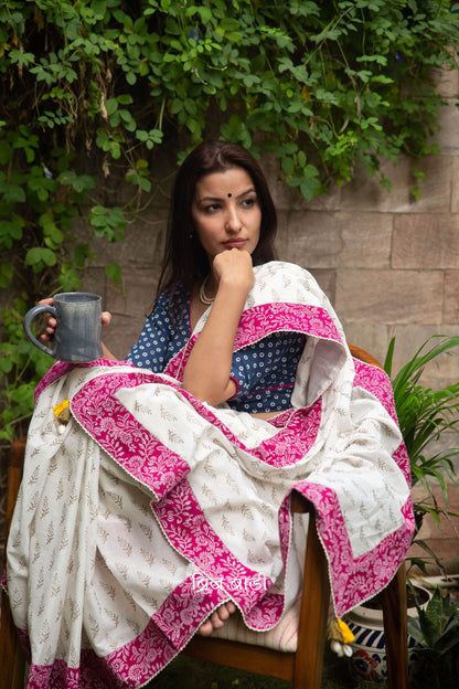 Off white soft cotton saree by Brij Bari hand block printed with intricate gold floral motifs & beautifully contrasted with a pink block printed border. Finished with delicate crochet detailing & adorned with yellow & light green handmade thread tassels accented with sea shells on pallu corner. Comes with matching block printed blouse piece. Perfect pick for festive or special occasions designed to make you stand out while staying effortlessly comfortable through long celebrations. Free shipping pan India