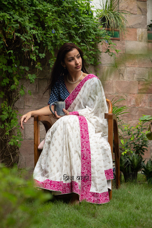 Off white soft cotton saree by Brij Bari hand block printed with intricate gold floral motifs & beautifully contrasted with a pink block printed border. Finished with delicate crochet detailing & adorned with yellow & light green handmade thread tassels accented with sea shells on pallu corner. Comes with matching block printed blouse piece. Perfect pick for festive or special occasions designed to make you stand out while staying effortlessly comfortable through long celebrations. Free shipping pan India